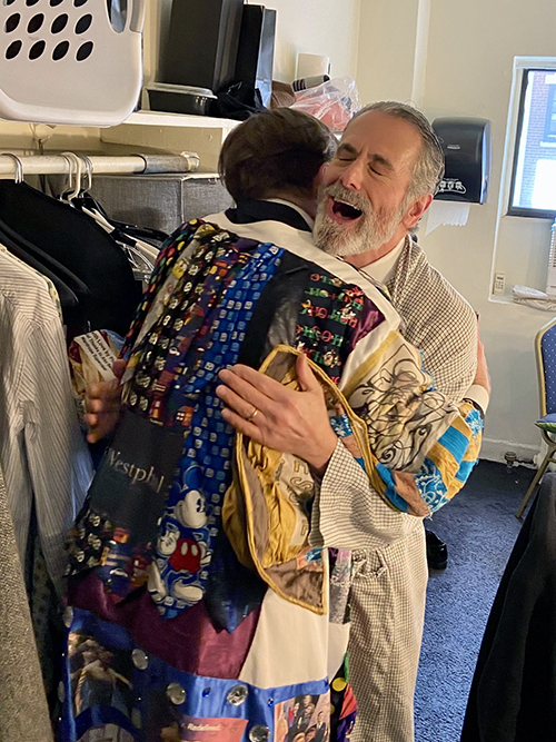 Cunliffe's back is visible as he embraces Steven Skybell in a dressing room. Skybell looks joyous.