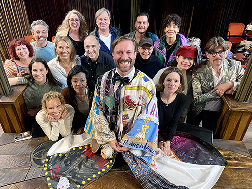 Cunliffe kneels onstage, the robe fanned out beneath him. Behind him pose fifteen other people, smiling at the camera.