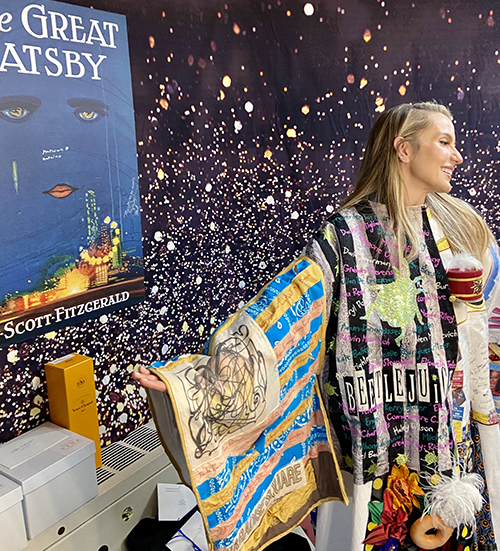 Webber poses in the Robe next to a poster that has the classic book cover for 'The Great Gatsby'