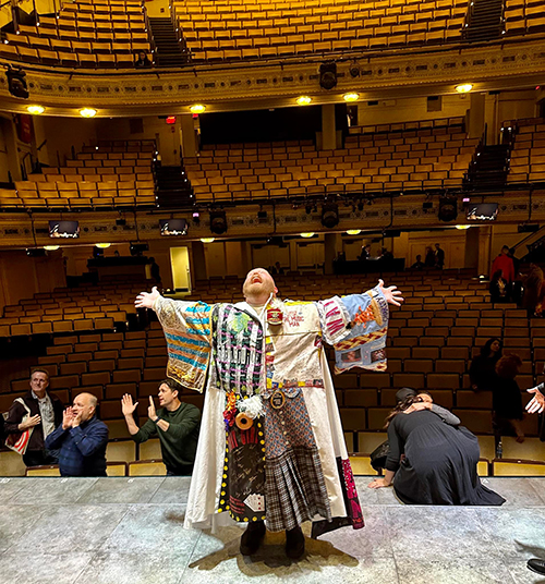 Jacob Keith Watson stands on stage wearing the Robe with his back to the seats, his head tilted back in joy.