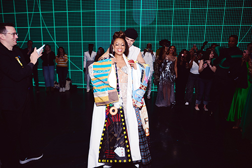 On a stage with a green background, A man standing behind Franklin puts the Robe on her, as several people around them applaud.