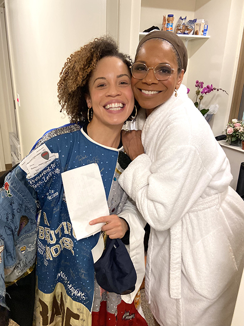 Hutchings in the Robe and Audra McDonald (in a dressing robe and wig cap), stand smiling backstage cheek to cheek.