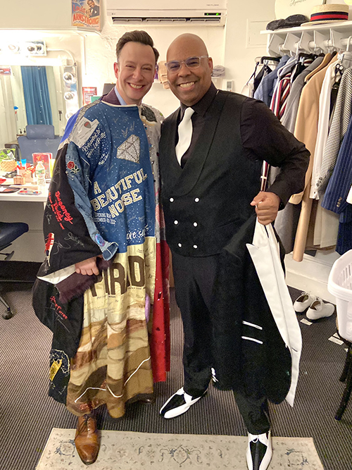 Sessions, wearing the Robe, stands backstage next to James Monroe Igelhart, who is holding his jacket in front of him. Both men are smiling.