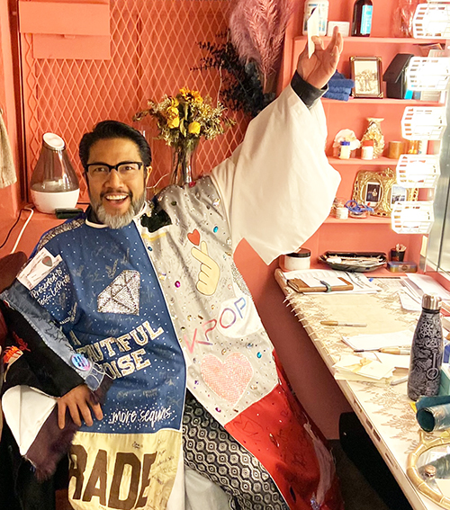 Robert Pendilla sits grinning in a dressing room in the Robe, one arm raised upwards.