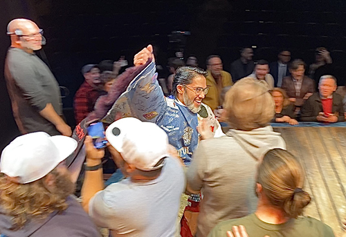 Pendilla is visible amidst a crowd of people onstage as he runs in the Robe. More people are visible crowded around the first row of the audience.